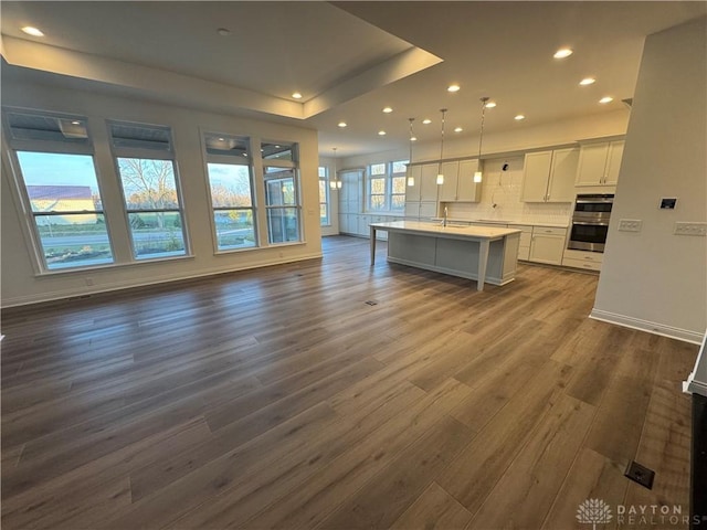 kitchen with dark hardwood / wood-style flooring, double oven, white cabinets, hanging light fixtures, and an island with sink