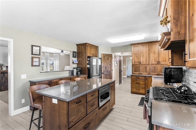 kitchen featuring stainless steel appliances, a kitchen bar, a kitchen island, ceiling fan, and tasteful backsplash