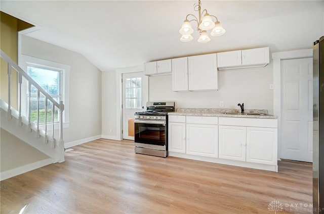 kitchen featuring stainless steel gas range, sink, pendant lighting, white cabinetry, and lofted ceiling