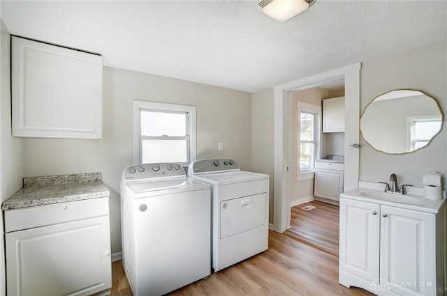 laundry area featuring washer and clothes dryer, sink, a healthy amount of sunlight, and light hardwood / wood-style flooring