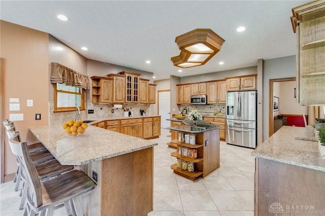 kitchen featuring decorative backsplash, kitchen peninsula, light stone counters, and stainless steel appliances