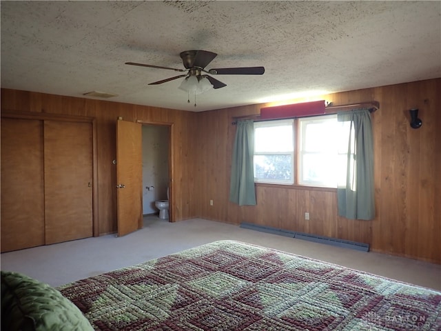 unfurnished bedroom with a baseboard radiator, a closet, ceiling fan, wooden walls, and connected bathroom