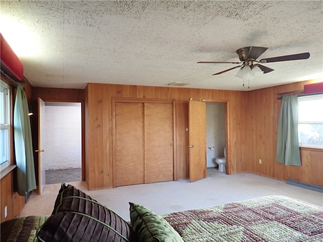 carpeted bedroom featuring ensuite bath, wood walls, a closet, and ceiling fan