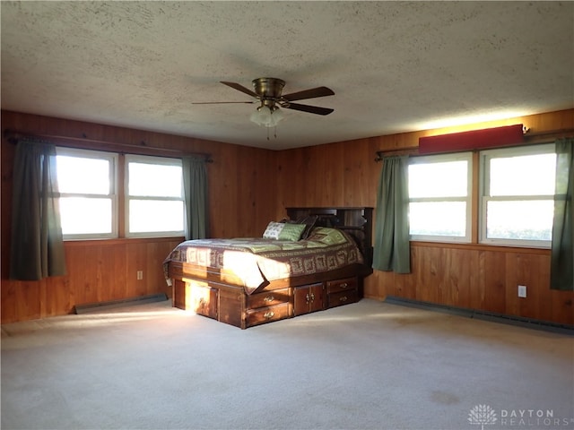 bedroom with wood walls, a textured ceiling, ceiling fan, light carpet, and baseboard heating