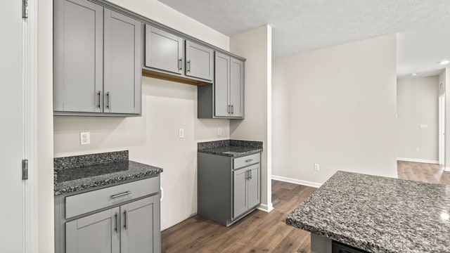 kitchen featuring a textured ceiling, gray cabinets, dark wood-type flooring, and dark stone countertops