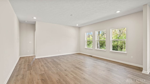 empty room with a textured ceiling and light hardwood / wood-style floors