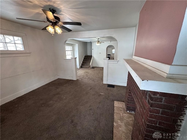 unfurnished living room featuring arched walkways, carpet flooring, plenty of natural light, and stairway