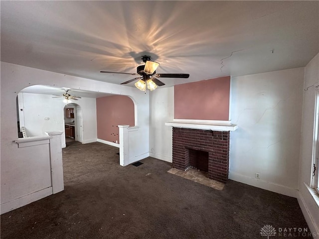 unfurnished living room with ceiling fan, dark carpet, and a brick fireplace