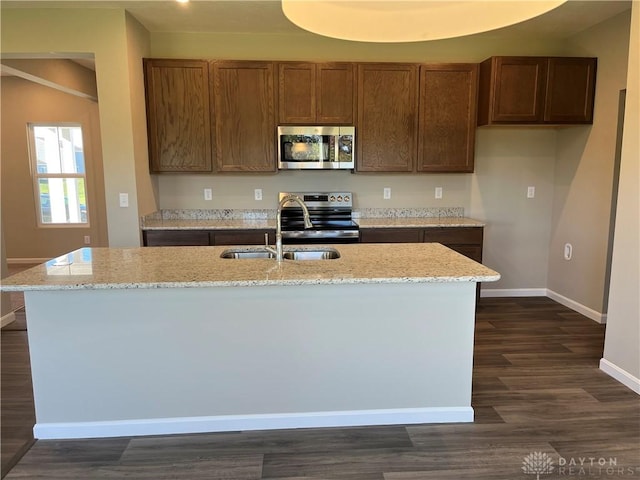 kitchen with a kitchen island with sink, sink, dark hardwood / wood-style floors, light stone countertops, and stainless steel appliances