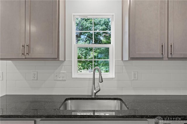 kitchen featuring backsplash, dark stone counters, and sink