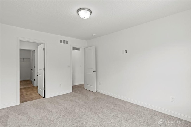 unfurnished bedroom with a walk in closet, a closet, and light carpet