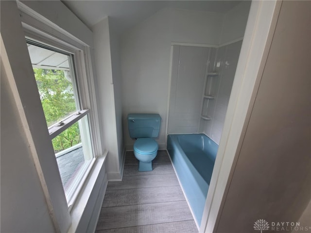 bathroom featuring hardwood / wood-style flooring, washtub / shower combination, and toilet