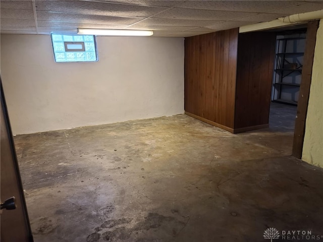 basement featuring a drop ceiling and wooden walls