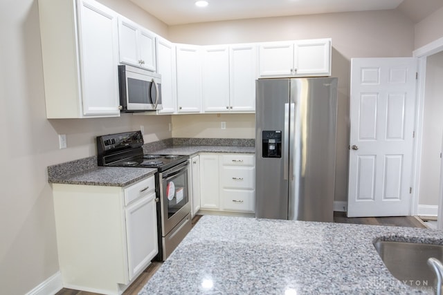 kitchen with appliances with stainless steel finishes, wood-type flooring, stone countertops, and white cabinets