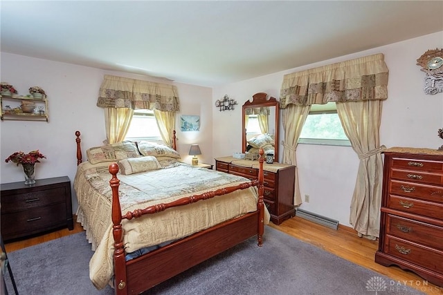 bedroom with hardwood / wood-style flooring, multiple windows, and a baseboard heating unit