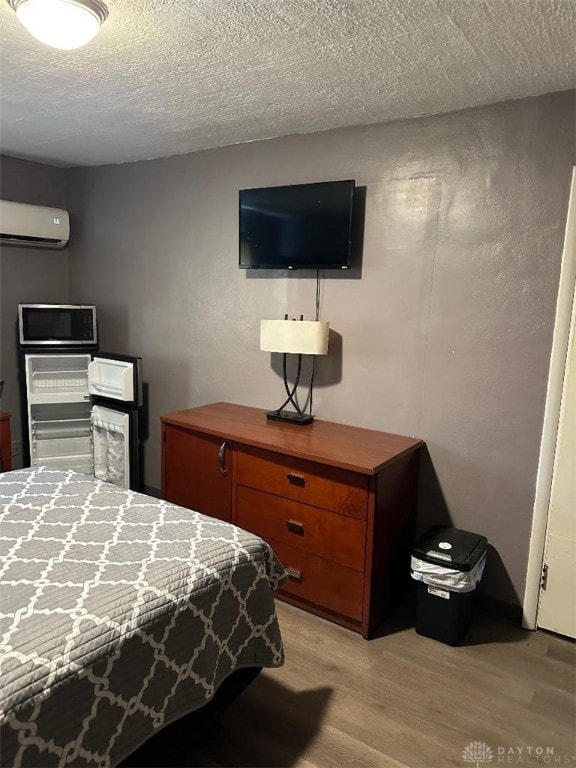 bedroom with a textured ceiling, a wall unit AC, and light hardwood / wood-style floors