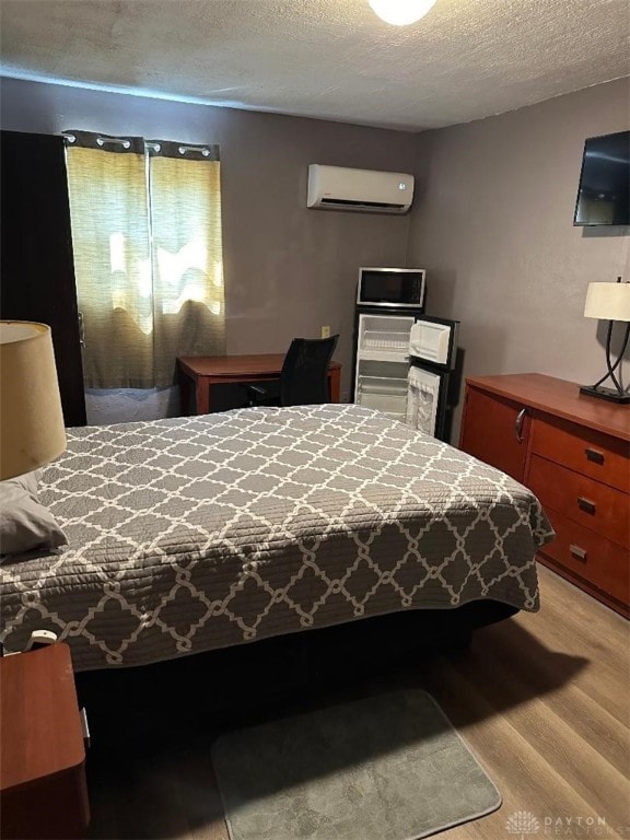 bedroom with a wall mounted AC, light hardwood / wood-style floors, and a textured ceiling