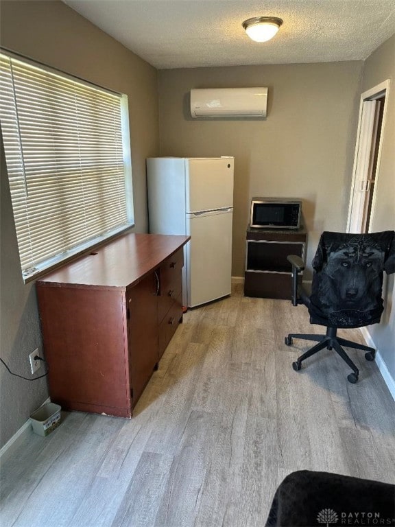 office area with a wall mounted AC, a textured ceiling, and light hardwood / wood-style floors