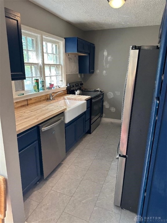 kitchen with wooden counters, a textured ceiling, stainless steel appliances, and blue cabinetry