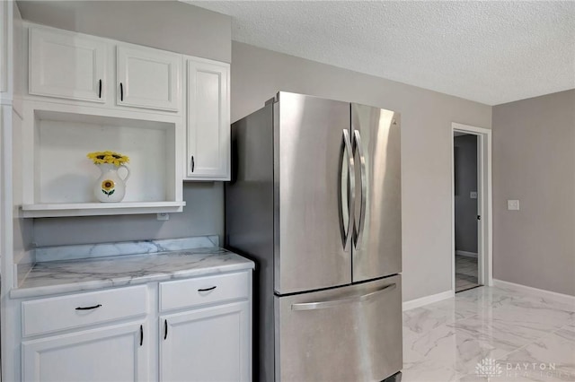 kitchen with white cabinetry, light stone countertops, stainless steel refrigerator, and a textured ceiling