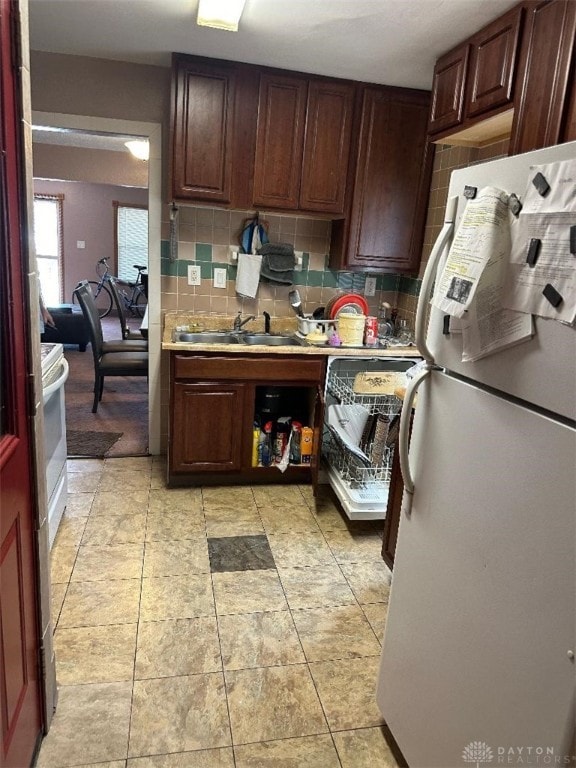 kitchen with light tile patterned floors, backsplash, sink, and white refrigerator