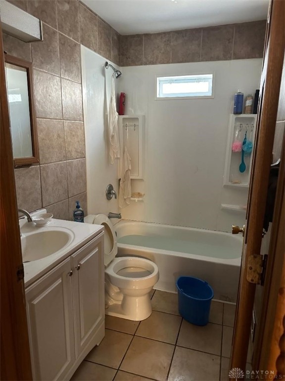 full bathroom with vanity, tile patterned floors, tiled shower / bath, tile walls, and toilet