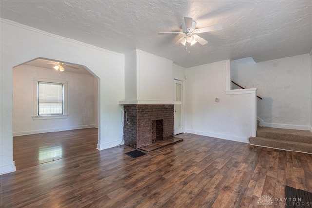 unfurnished living room with a textured ceiling, a brick fireplace, dark hardwood / wood-style floors, ceiling fan, and ornamental molding