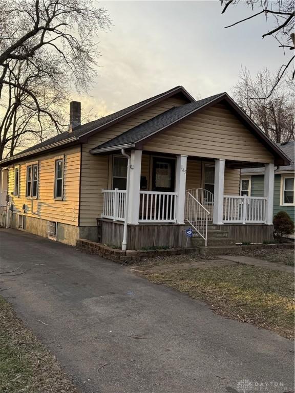 view of front of house with aphalt driveway, covered porch, and a chimney