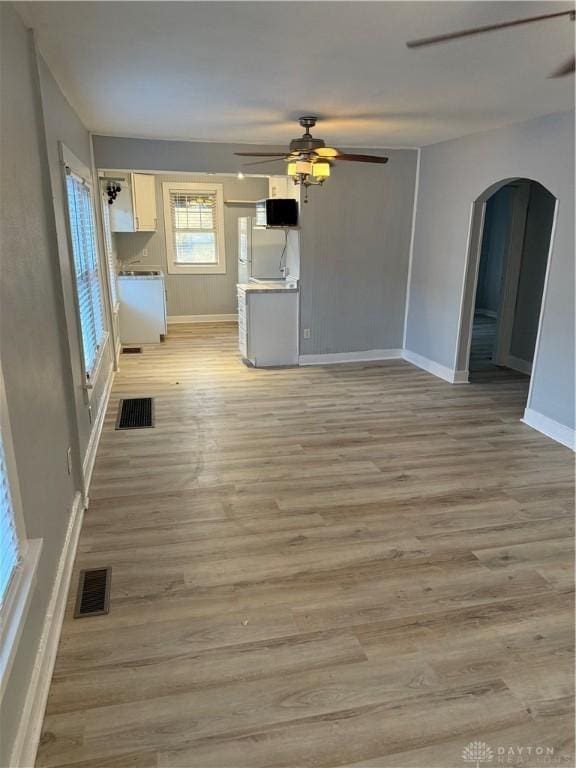 unfurnished living room featuring light wood-style floors, visible vents, arched walkways, and ceiling fan