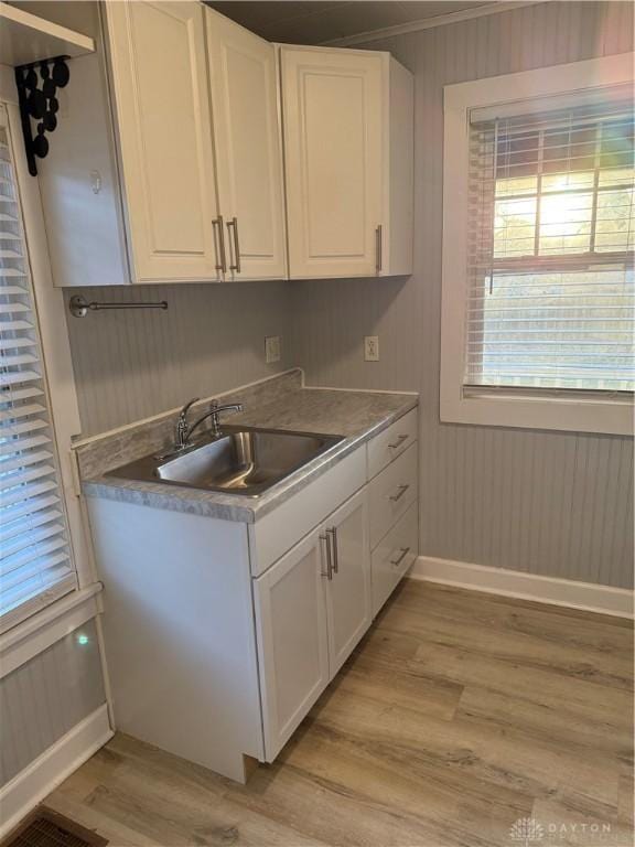 kitchen featuring baseboards, light wood-type flooring, ornamental molding, white cabinets, and a sink