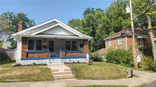 bungalow-style home with a porch, a chimney, and a front lawn