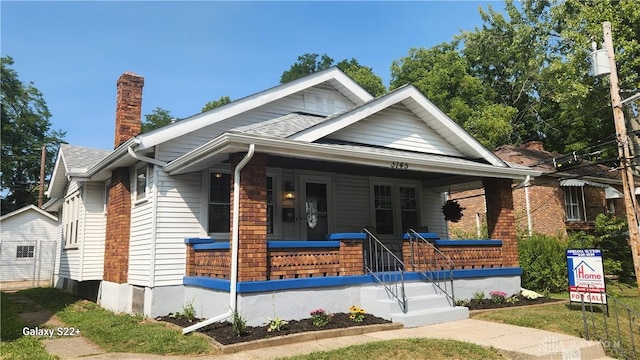 bungalow-style home with covered porch, a chimney, and roof with shingles