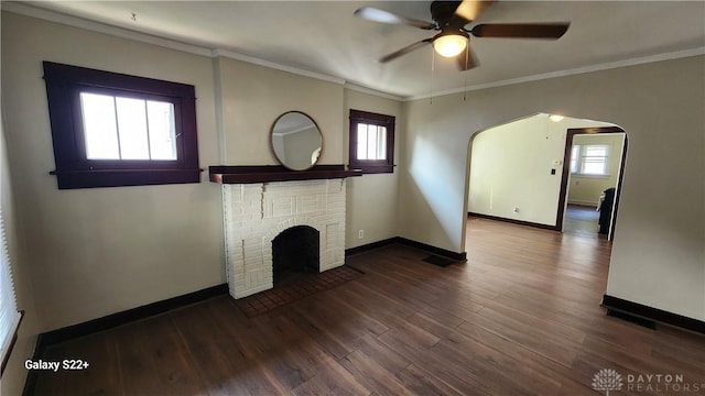 unfurnished living room featuring baseboards, arched walkways, dark wood-style floors, ornamental molding, and a brick fireplace