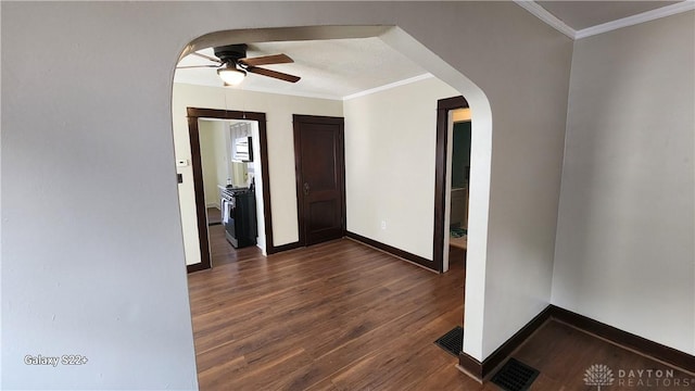 empty room featuring baseboards, arched walkways, ceiling fan, dark wood-style flooring, and crown molding