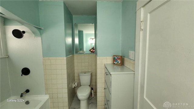 bathroom with a tub to relax in, a wainscoted wall, tile walls, and toilet