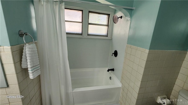 full bath featuring shower / tub combo, tile walls, and a wainscoted wall