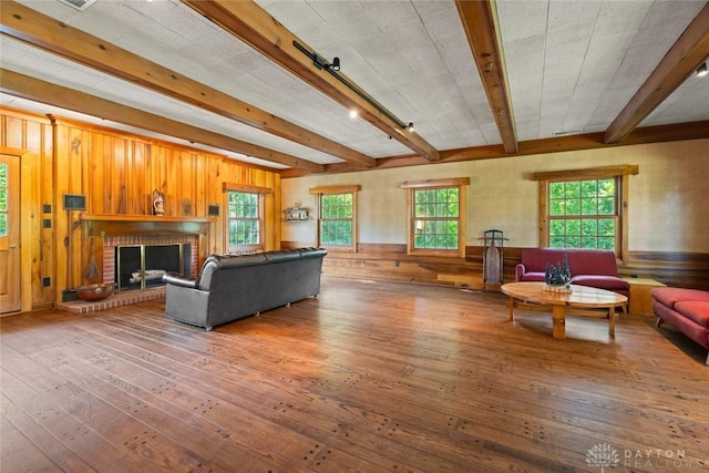 living area featuring beam ceiling, wood walls, a brick fireplace, and hardwood / wood-style flooring