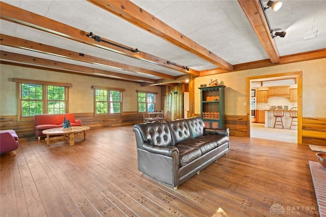 living area with a wainscoted wall, beam ceiling, and hardwood / wood-style floors