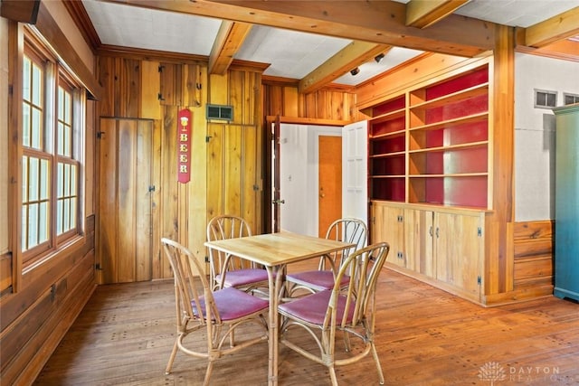 dining room with wood walls, plenty of natural light, and beam ceiling