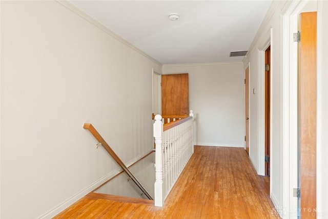 hallway with light wood-style floors, visible vents, ornamental molding, and an upstairs landing