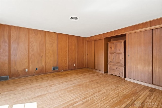 unfurnished room with light wood-style floors, visible vents, and wood walls