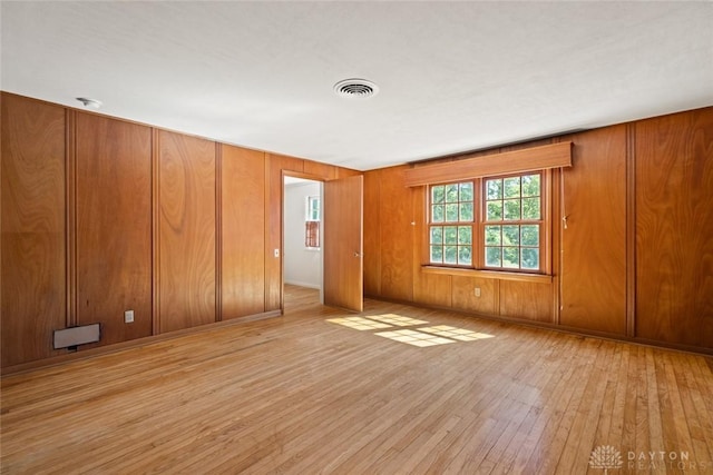 unfurnished bedroom with wood-type flooring, visible vents, and wooden walls