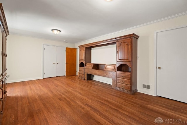 unfurnished bedroom featuring baseboards, crown molding, visible vents, and wood finished floors