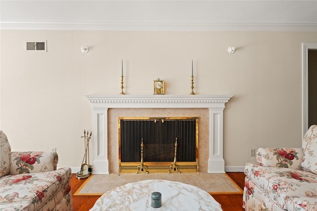 living area featuring a fireplace with flush hearth, wood finished floors, visible vents, baseboards, and ornamental molding