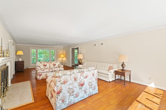 living area with a tiled fireplace, wood finished floors, visible vents, and crown molding