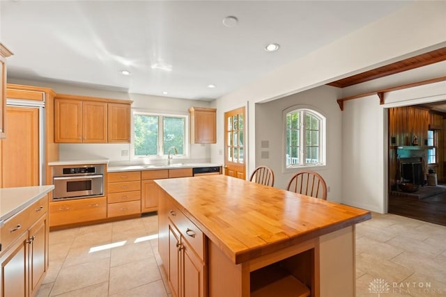 kitchen featuring light tile patterned flooring, butcher block counters, a sink, stainless steel oven, and a center island