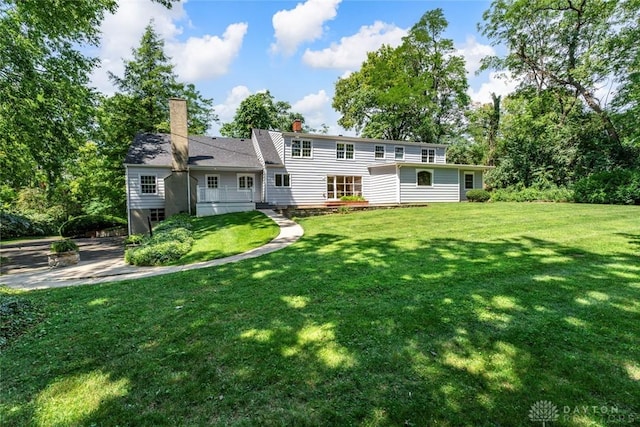 back of property with a wooden deck, a chimney, and a yard