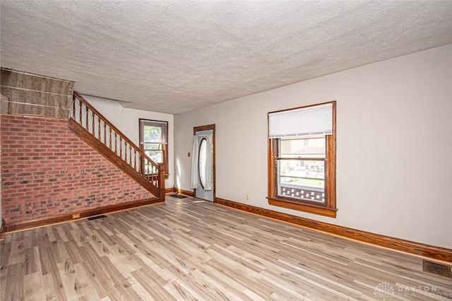 unfurnished living room featuring light hardwood / wood-style flooring, a textured ceiling, and brick wall