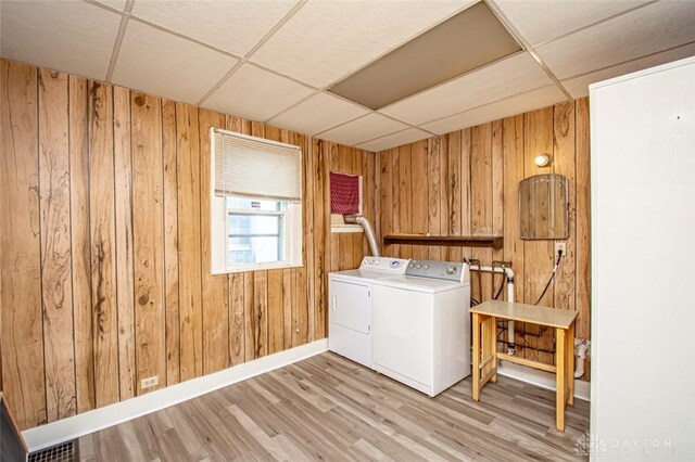 laundry room featuring light wood-type flooring, separate washer and dryer, and wooden walls