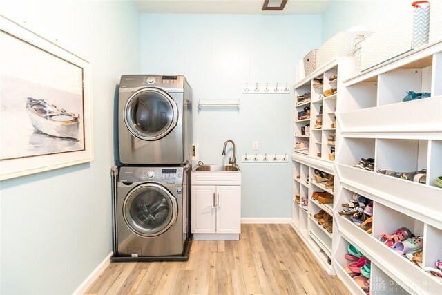 clothes washing area featuring cabinets, stacked washing maching and dryer, light hardwood / wood-style floors, and sink